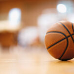 Close-up image of basketball ball over floor in the gym. Orange basketball ball on wooden parquet.