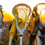 Girls women's lacrosse sticks in air at sunset